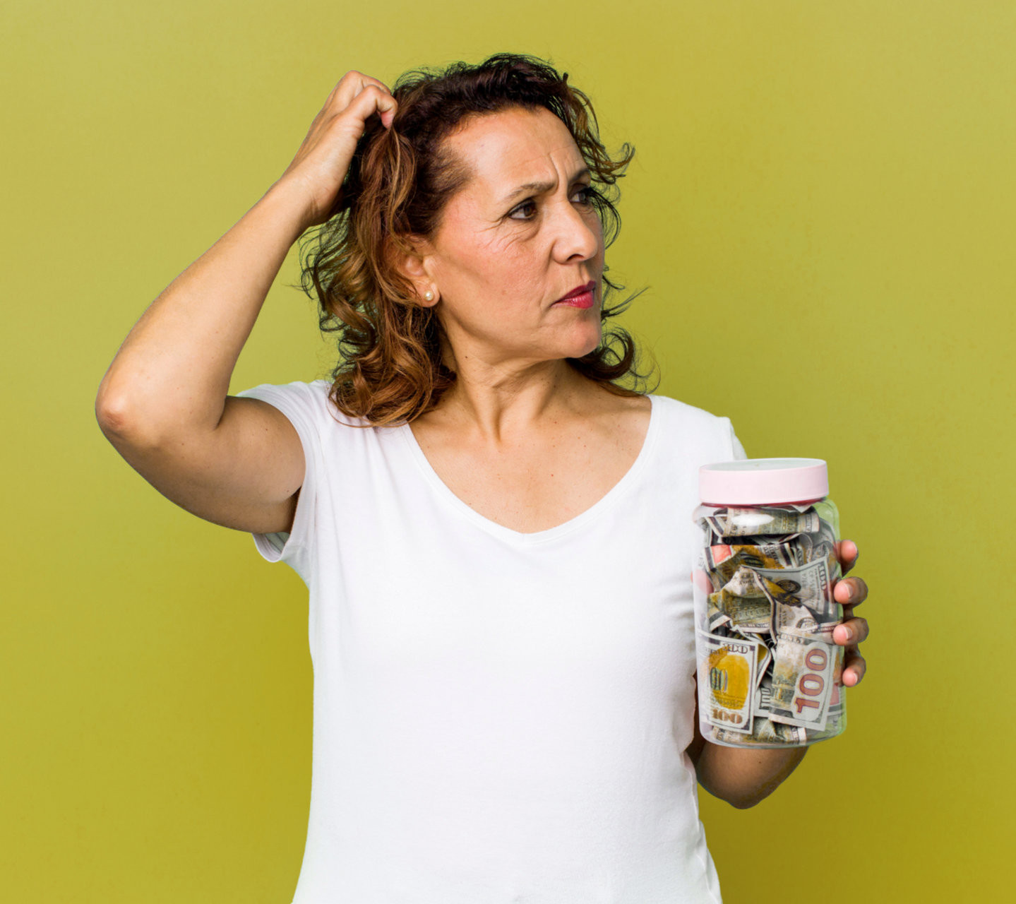 Verwirrte Frau hält ein Glas voller Geldscheine und kratzt sich fragend am Kopf – Symbol für die Überforderung mit Finanzthemen, die die Finanz Fach Frauen mit klarer, verständlicher Beratung auflösen.