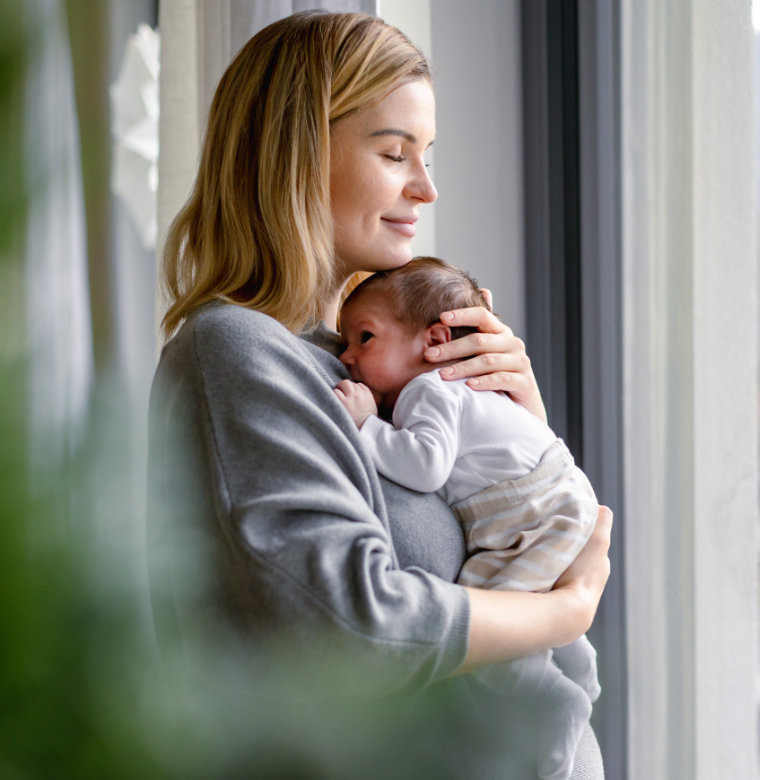 Mutter hält ihr Baby am Fenster – steht für Familienfinanzen, Vorsorge und finanzielle Sicherheit für die Zukunft.