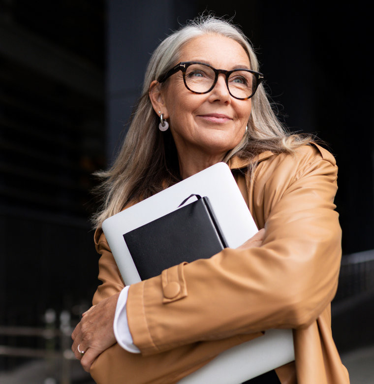 Frau mit grauem Haar hält Laptop und Notizbuch – steht für kluge Finanzentscheidungen in neuen Lebenssituationen.